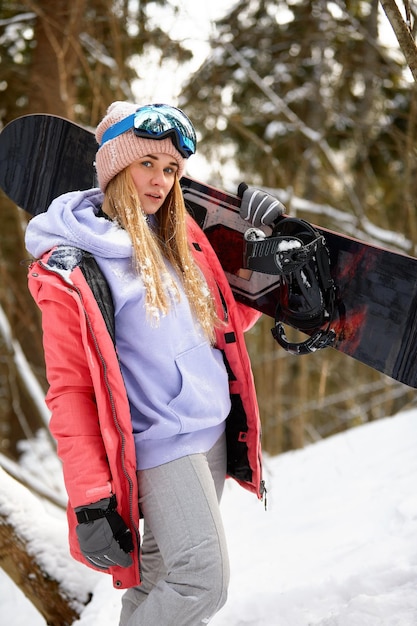 Snowboardzista kaukaski kobieta trzyma snowboard na tle pięknego śnieżnego lasu w słoneczny dzień