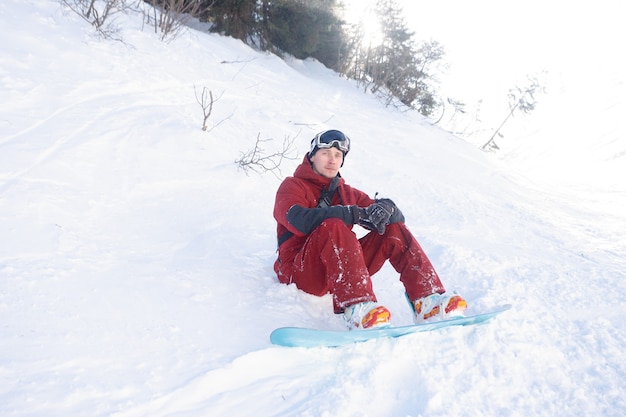 snowboardzista siedzi wysoko w górach na skraju stoku i spogląda w dal.