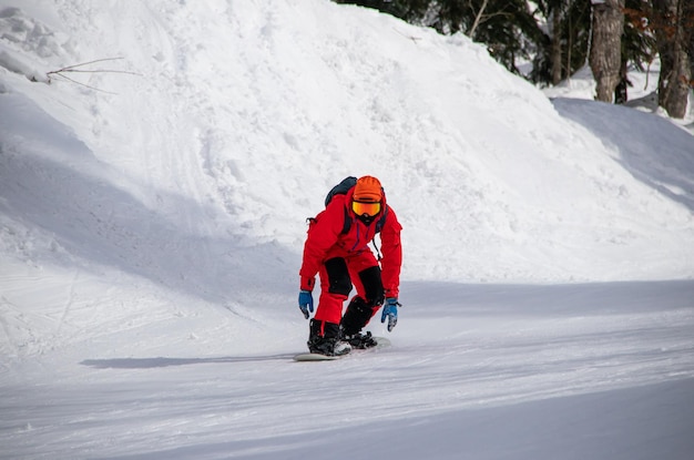 Snowboardzista w czerwonym kombinezonie jeździ leśnym torem w górach