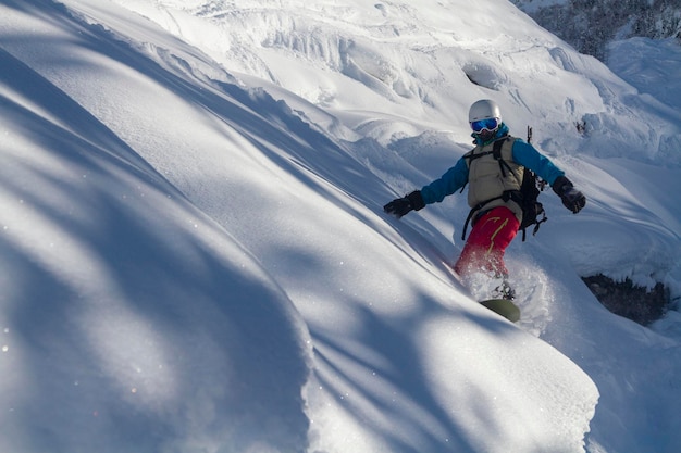 Snowboardzista w masce narciarskiej i kasku schodzi z miękkich śnieżnych wzgórz rozpraszających śnieg