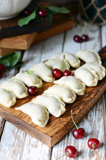 Soczyste pierogi ze świeżymi wiśniami na drewnianej desce do krojenia. Wizerunek surowe pierogi ze świeżymi wiśniami na białym stole rustykalnym. Rustykalny. Danie narodowe. Widok z góry.