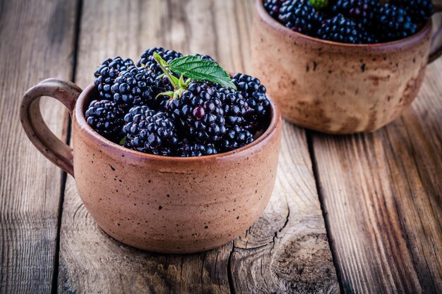 Zdjęcie soczyste świeże organiczne jeżyny w kubkach na drewnianym tle