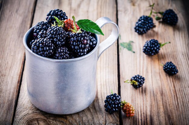 Soczyste świeże organiczne jeżyny w starym kubku na drewnianym tle