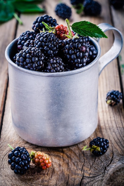 Soczyste świeże organiczne jeżyny w starym kubku na drewnianym tle