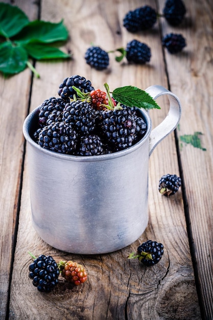 Soczyste świeże organiczne jeżyny w starym kubku na drewnianym tle