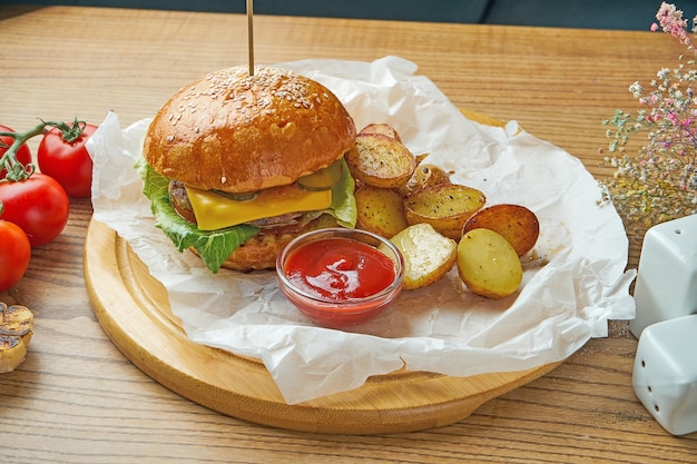 Soczysty burger z wołowiną, topionym serem, ogórkiem i dekoracją z młodych ziemniaków na pergaminie. Amerykańskie fast foody