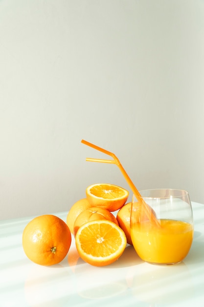 Sok pomarańczowy w szklance otoczony naturalnymi pomarańczami z naturalnym światłem słonecznym na białym tle
