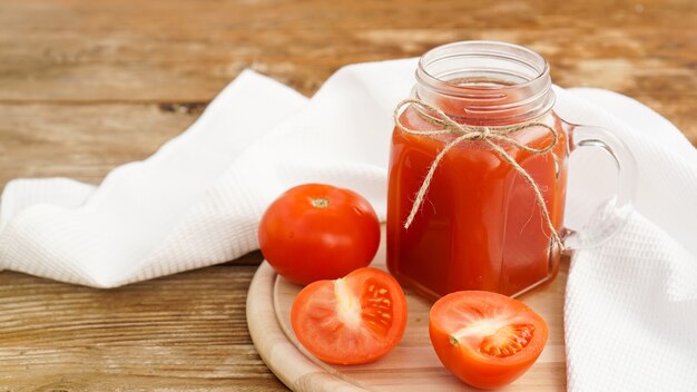 Sok pomidorowy w szklanym słoju i świeże pomidory na drewnianym