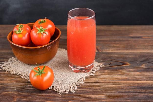 Sok pomidorowy z pomidorami na tle czarnym i drewnianym.