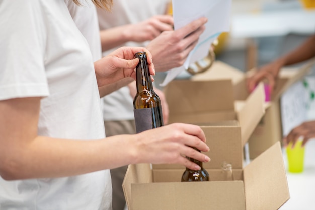 Sortowanie Odpadów. Ręce Układające Puste Szklane Butelki W Pudełku Kartonowym W Centrum Recyklingu