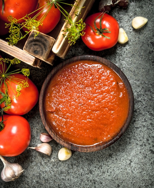 Sos pomidorowy z przyprawami i czosnkiem w misce. Na tle rustykalnym.