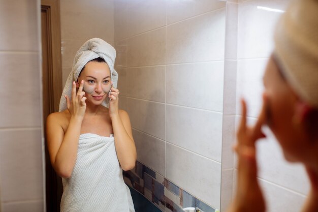 Spa i kosmetologia pielęgnacja skóry twarzy w domu dziewczyna w łazience nakłada kremową maskę na twarz