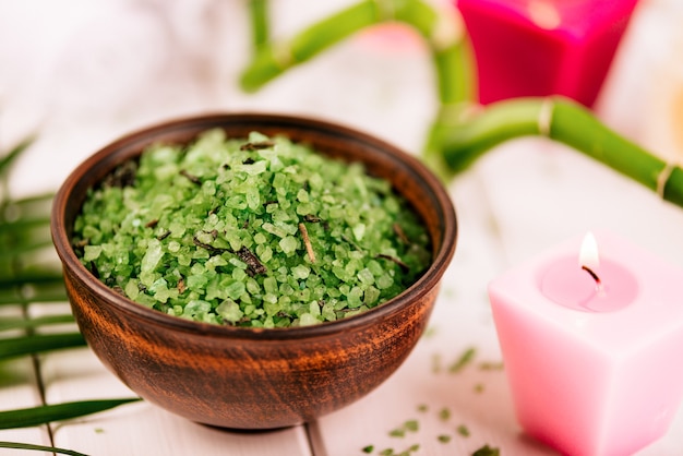 Spa. Zielona ziołowa sól spirulina w ceramicznej misce, ręczniki spa, różowa świeca zapachowa i bambus. Stonowany, matowy.