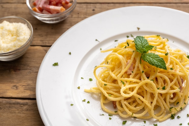 Spaghetti a la carbonara na białym talerzu i rustykalnym stole