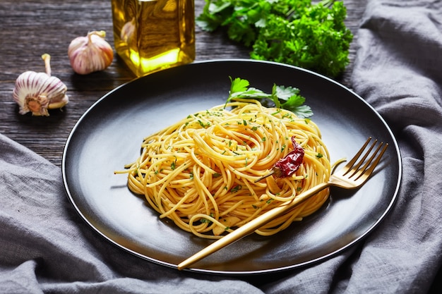 Spaghetti Alla colatura di alici, Spaghetti polane sosem anchois, papryczką pimentową, czosnkiem i natką pietruszki na czarnym talerzu ze złotym widelcem na ciemnym drewnianym stole, widok na krajobraz