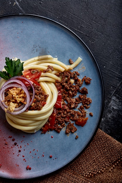 Spaghetti bolognese. Koncepcja włoskiej kuchni, spaghetti pięknie ułożone na talerzu i podlane sosem bolońskim. Niebieski talerz, ciemna powierzchnia. Widok z góry