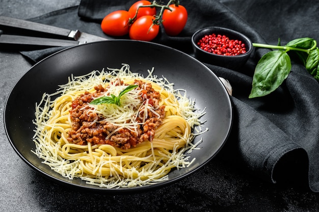 Spaghetti bolognese z pomidorami i mielonym mięsem, parmezanem i bazylią. Czarne tło. Widok z góry