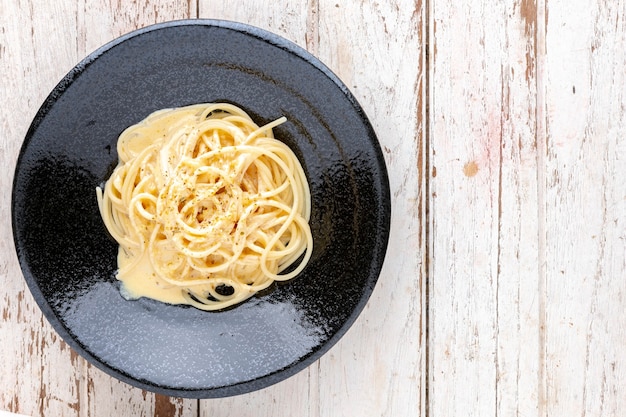 Spaghetti carbonara z kremowym sosem i oregano na wierzchu w czarnej płycie ceramicznej na białym tle starego drewna tekstury z kopią miejsca na tekst, widok z góry