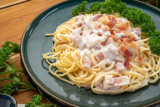 Spaghetti carbonara z szynką i boczkiem na zielonym talerzu na drewnianym stole