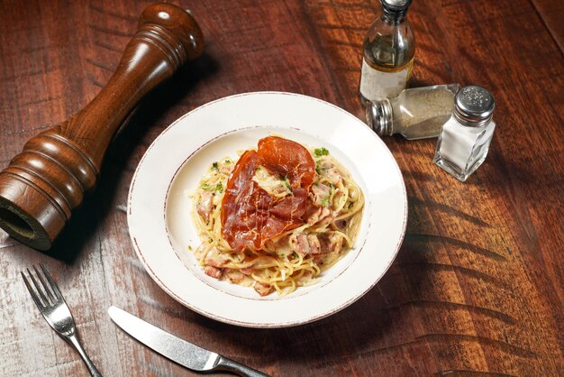 Spaghetti Carbonara z szynką i serem podawane w naczyniu izolowanym na drewnianym blacie widok włoskiego fast foodu