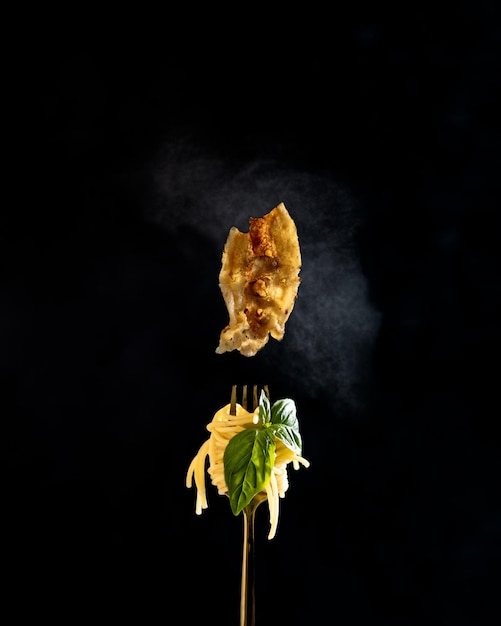 Spaghetti z bazylią na widelcu Gorący latający boczek z parą wokół Pionowo na czarnym tle