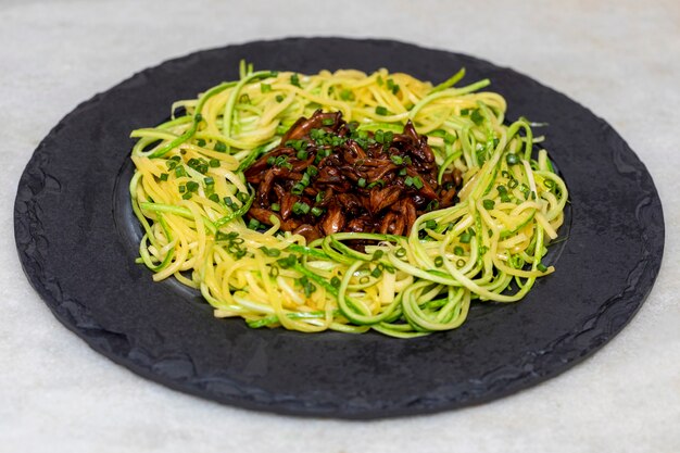 Spaghetti z cukinii z shimeji na czarnej kamiennej płycie.