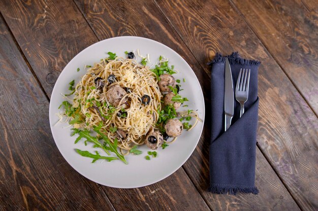 Spaghetti z klopsikami oliwki i rukolą na drewnianym stole