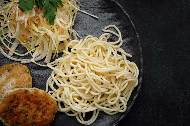 Spaghetti z kotletem i surówką na czarnym talerzu