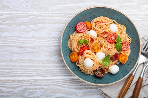 Spaghetti z mozzarellą kolorowe pomidory koktajlowe ze świeżą bazylią na talerzu ceramicznym