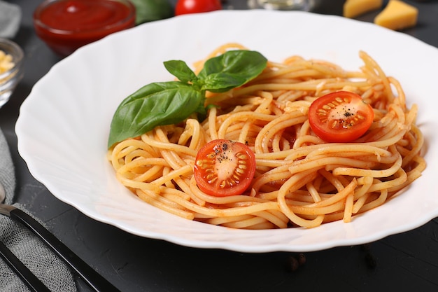 Spaghetti z sosem pomidorowym i pomidorkami koktajlowymi z bazylią na białym talerzu na ciemnym tle