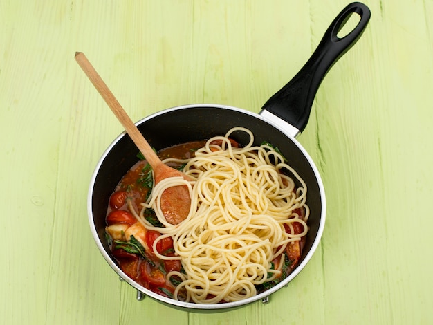 Zdjęcie spaghetti z sosem pomidorowym i ziołami na patelni