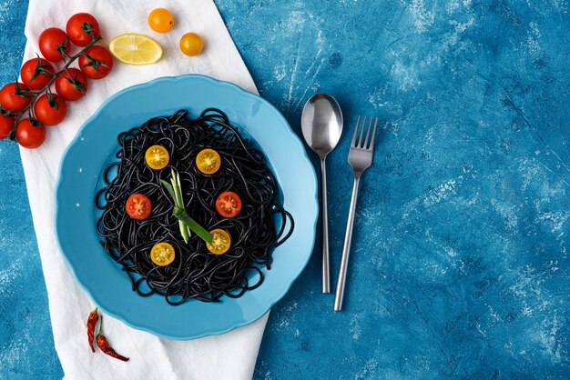 Spaghetti Z Tuszem Mątwy Z żółtymi I Czerwonymi Pomidorkami Cherry Na Niebieskim Talerzu Na Niebieskim Tle Z Miejsca Na Kopię