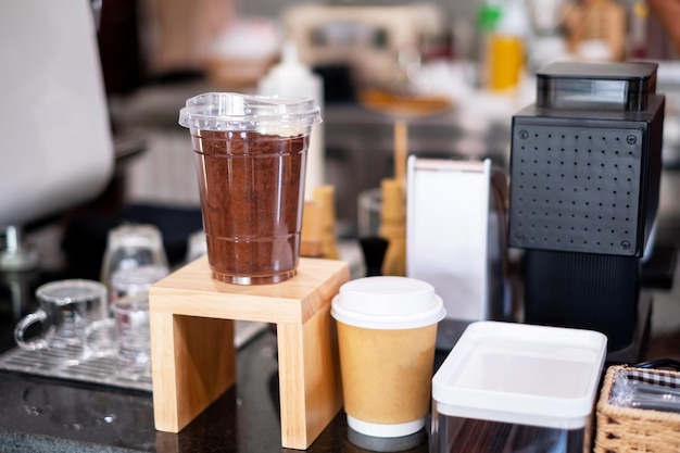 Spalony brązowy proszek kawy w przezroczystym plastikowym kubku do kawy siedzi na drewnianym liczniku w pobliżu kasy, aby wyświetlić próbkę towarów z kawiarni