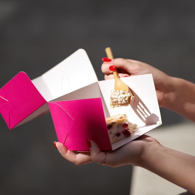 Spalony sernik z bliska na różowym pudełku na wynos w rękach kobiet