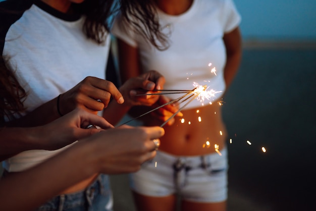 Sparklers w rękach młodych dziewcząt na plaży. Trzy dziewczyny cieszą się imprezą na plaży z sparklers. Wakacje letnie, wakacje, relaks i styl życia koncepcji.