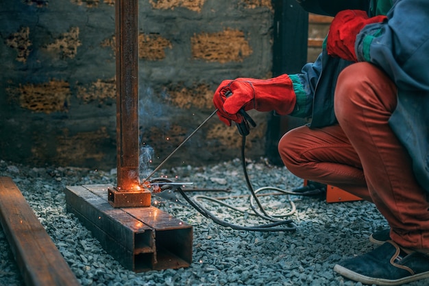 Spawacz zgrzewa metalową rurę spawaniem elektrycznym, trzyma w rękach elektrodę