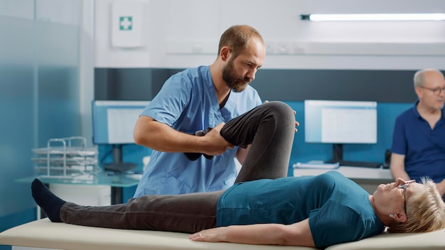 Specjalista ds. zdrowia stosujący procedurę podniesienia nogi w celu złamania kości podczas wizyty u starego pacjenta w osteopatii. Fizjoterapeuta wykonujący rozciąganie fizyczne w celu leczenia kontuzji podczas rehabilitacji.