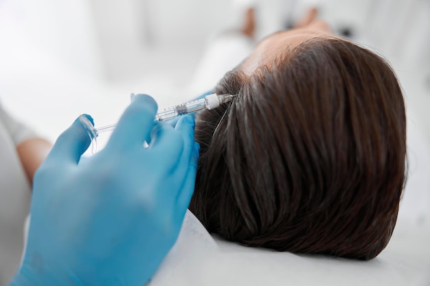 Specjalista wykonuje iniekcje w skórę głowy pacjenta podczas zabiegu mezoterapii w poradni kosmetologicznej
