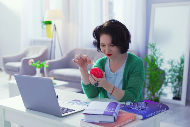 Specjalna świeca. Miła miła kobieta trzyma czerwoną świecę siedząc w swoim miejscu pracy