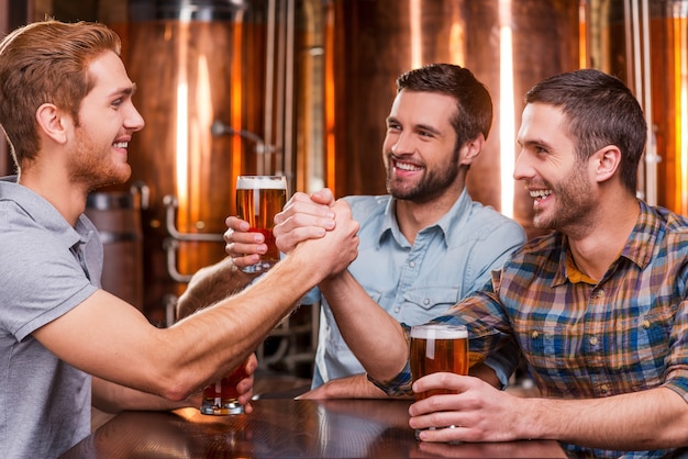 Spędzanie wspaniałego czasu z przyjaciółmi. Trzech szczęśliwych młodych mężczyzn w swobodnym piciu piwa, siedząc razem w pubie piwnym