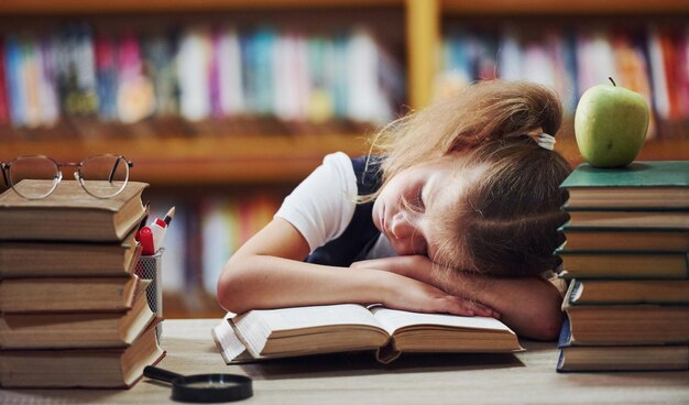 Śpi na stole Słodka dziewczynka z włosami jest w bibliotece Jabłko na książkach