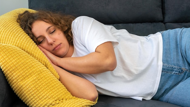 Śpiąca kobieta z kręconymi włosami drzemiąca na kanapie w ciągu dnia w przytulnym mieszkaniu Atrakcyjna dziewczyna śpi leżąc na wygodnej kanapie z zamkniętymi oczami Koncepcja marzeń i odpoczynku
