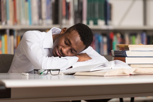 Śpiący afrykański student siedzący i oparty na stosie książek w college'u Mała głębia ostrości
