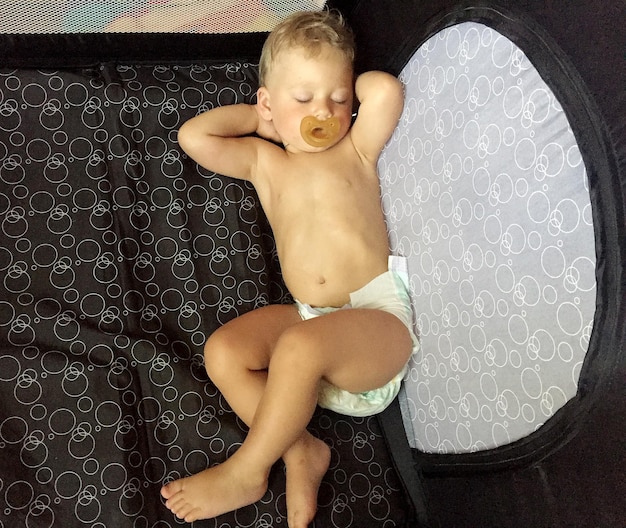 Zdjęcie Śpiący chłopiec z pacifierem dla dziecka pozujący fotograf na kolorowe zdjęcie