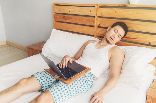 Śpiący mężczyzna pracuje ze swoim laptopem na wygodnym łóżku