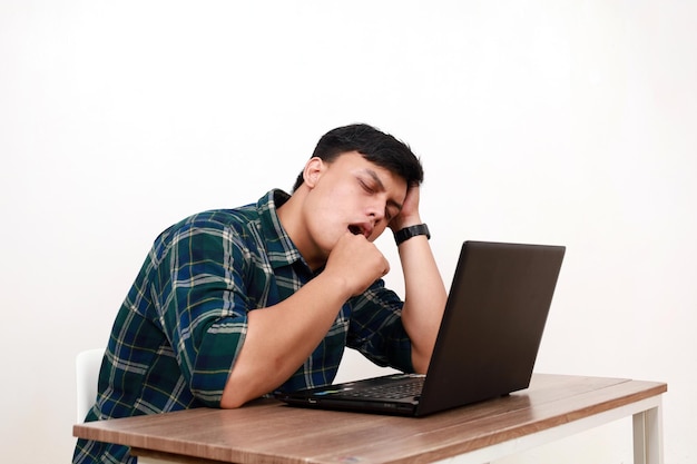 Śpiący młody azjatycki student siedzący z laptopem na biurku.