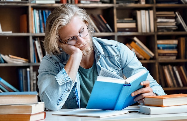 Śpiący zmęczony student w bibliotece przy biurku do egzaminu