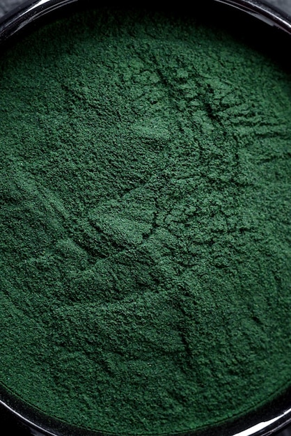 Spirulina w kolorze zielonym w postaci proszku w czarnej misce na ciemnym betonowym tle