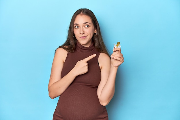 Spodziewająca się kobieta trzymająca gryzak dla niemowląt w niebieskim studio