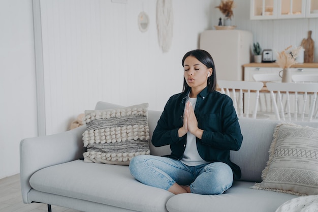 Spokojna kobieta oddycha ćwicząc jogę siedząc w pozycji lotosu na kanapie w domu Wellness odprężenie